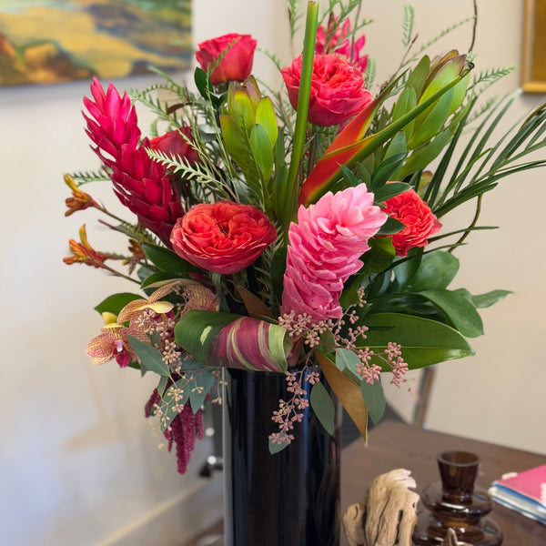 Tropical design with clustered, spilling foliage, black cylinder vase