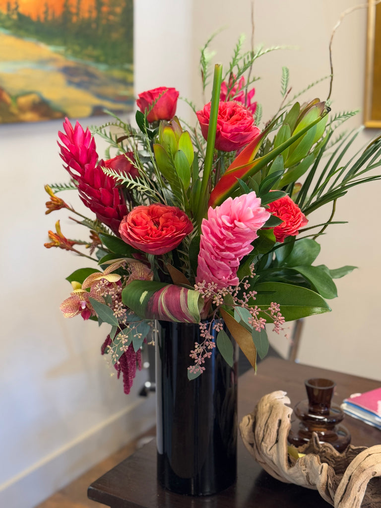 Tropical design with clustered, spilling foliage, black cylinder vase